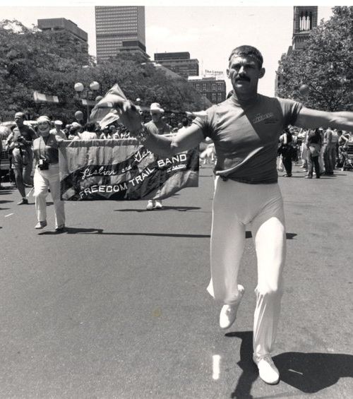A man twirls a baton and marches in the 1985 Pride Parade in front of a banner for the Lesbian and Gay Freedom Trail Band. Credit: Susan Fleischmann