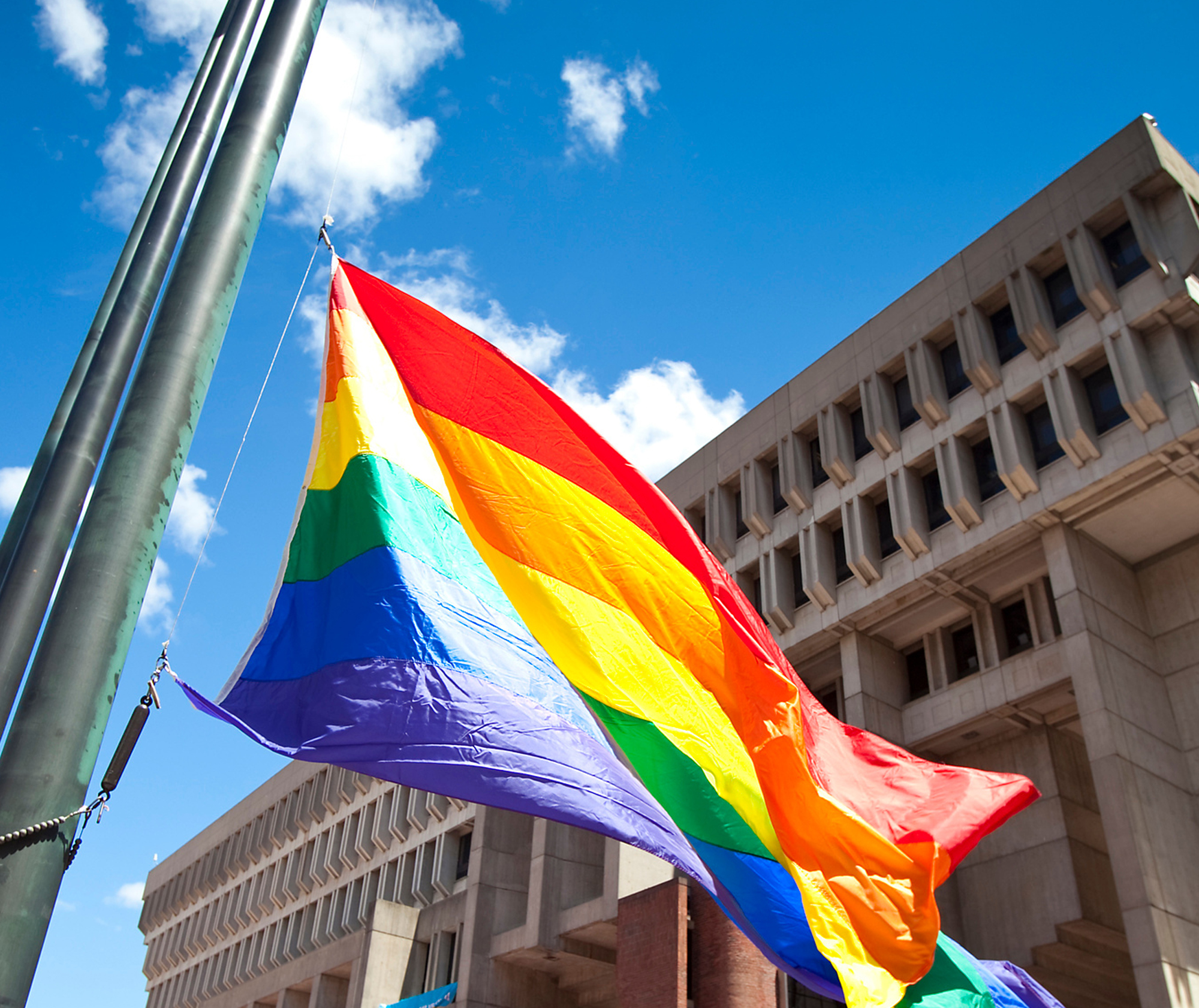 Rainbow Flag blowing in the wind with Boston City Hall in the background.